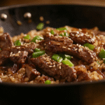 Closeup of homemade onion beef fried rice with tender beef strips, caramelized onions, green onions, and toasted sesame seeds in a cast iron skillet